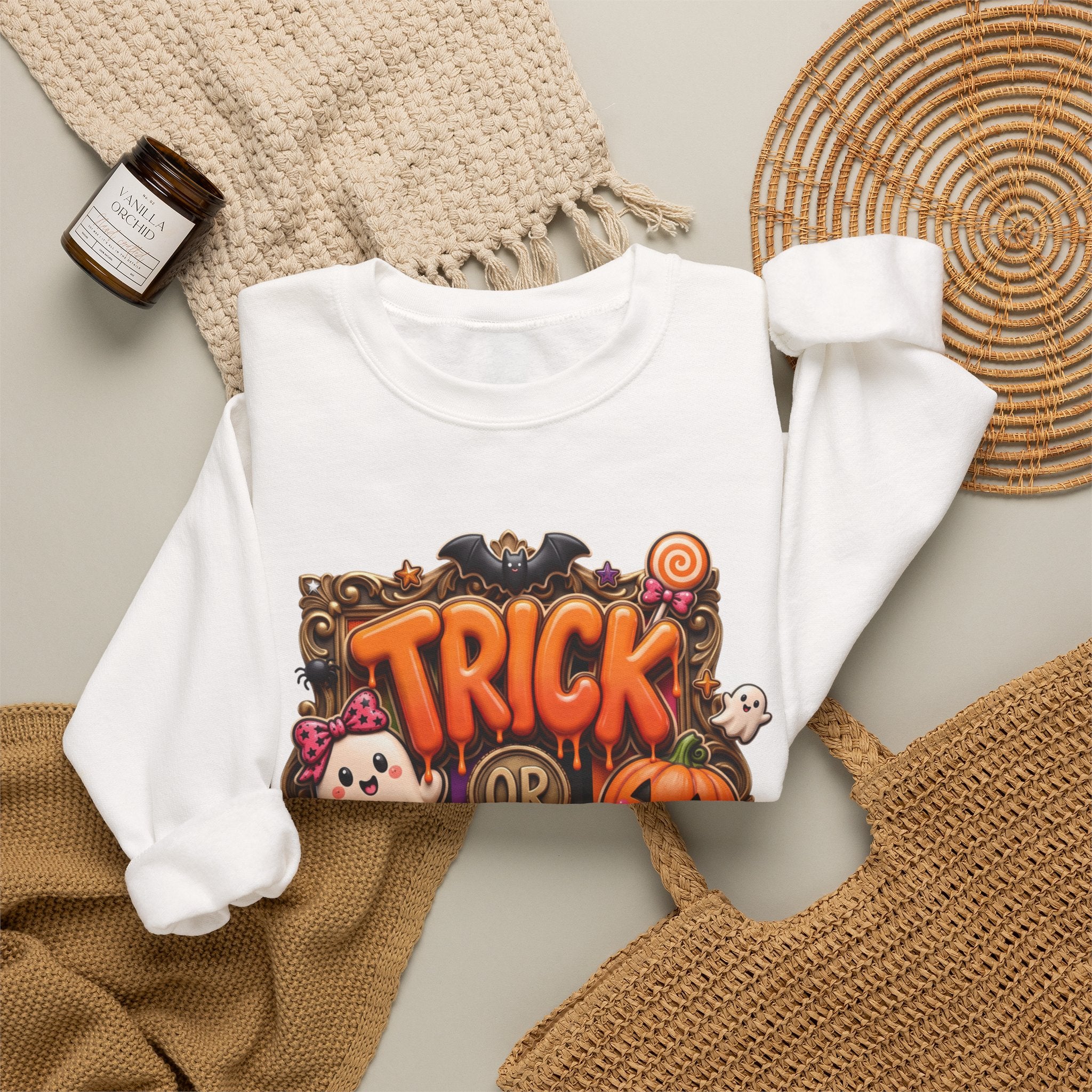 White crewneck sweatshirt styled flat with a candle — puffy orange trick or treat lettering