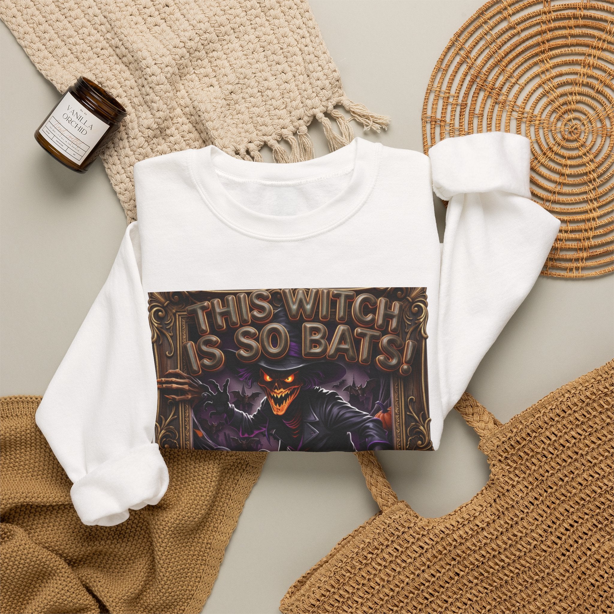 White crewneck sweatshirt styled flat with a candle — grinning witch in a pointed hat