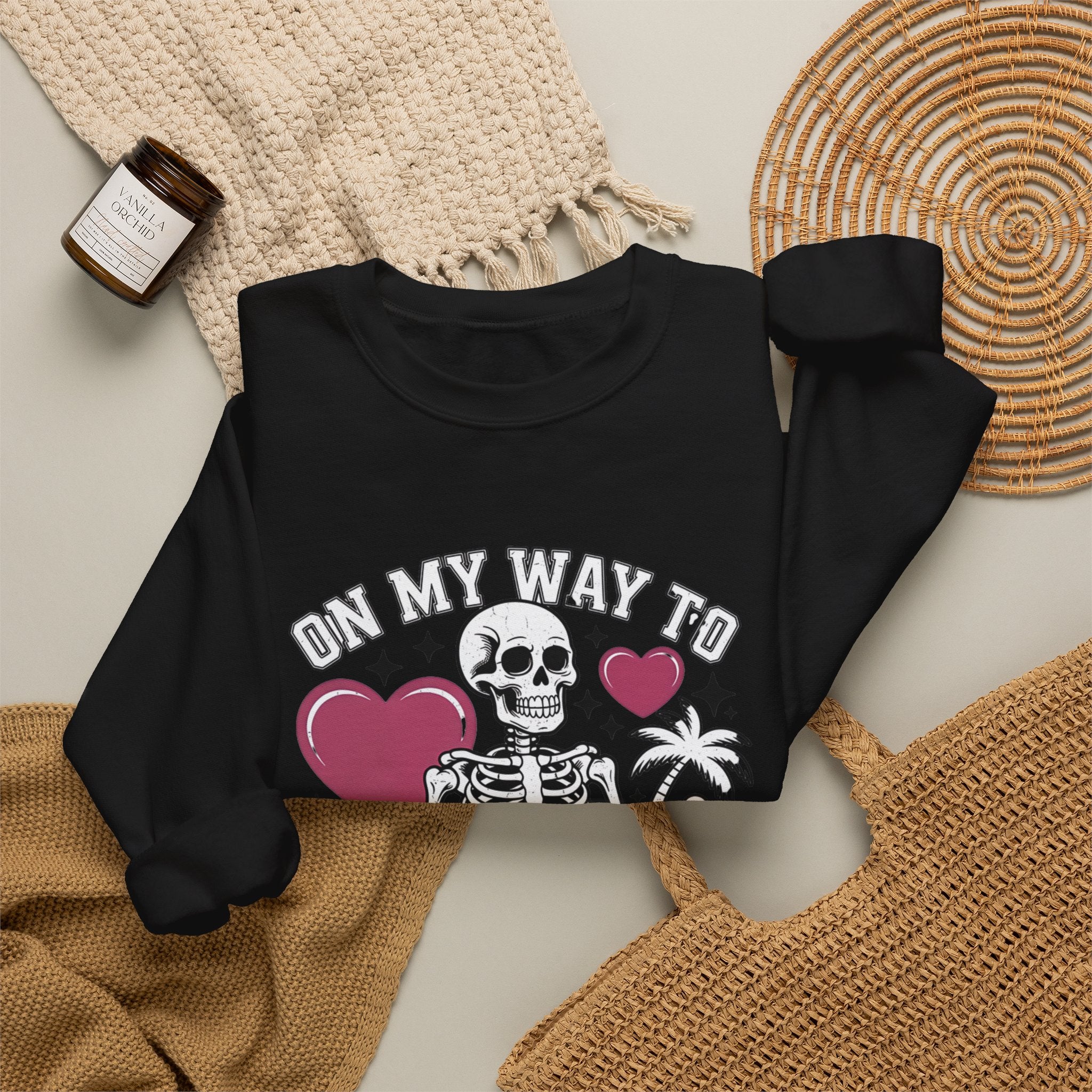 Black crewneck sweatshirt styled flat with a candle — line-drawn skeletons under pink hearts