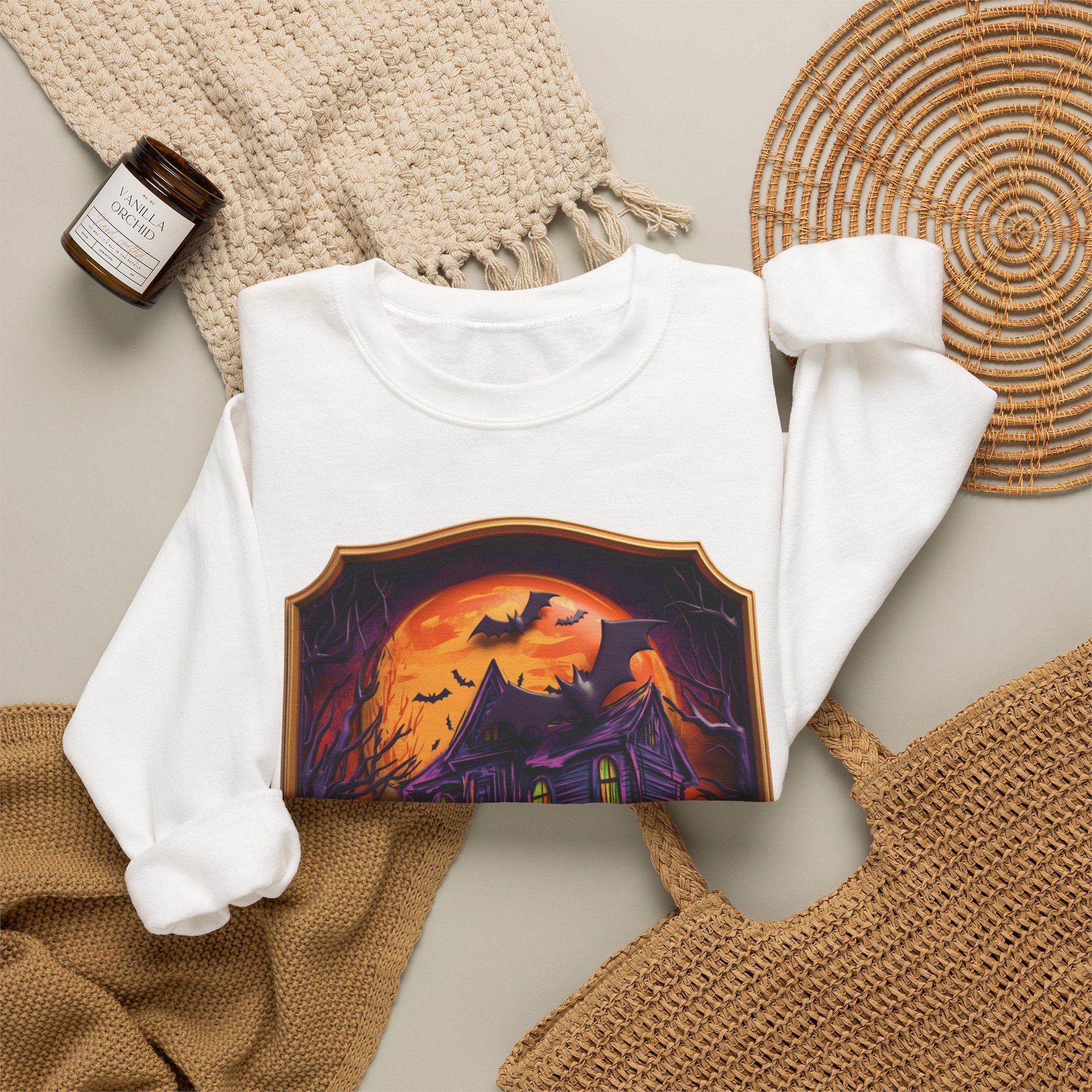 White crewneck sweatshirt styled flat with a candle — haunted mansion under an orange moon