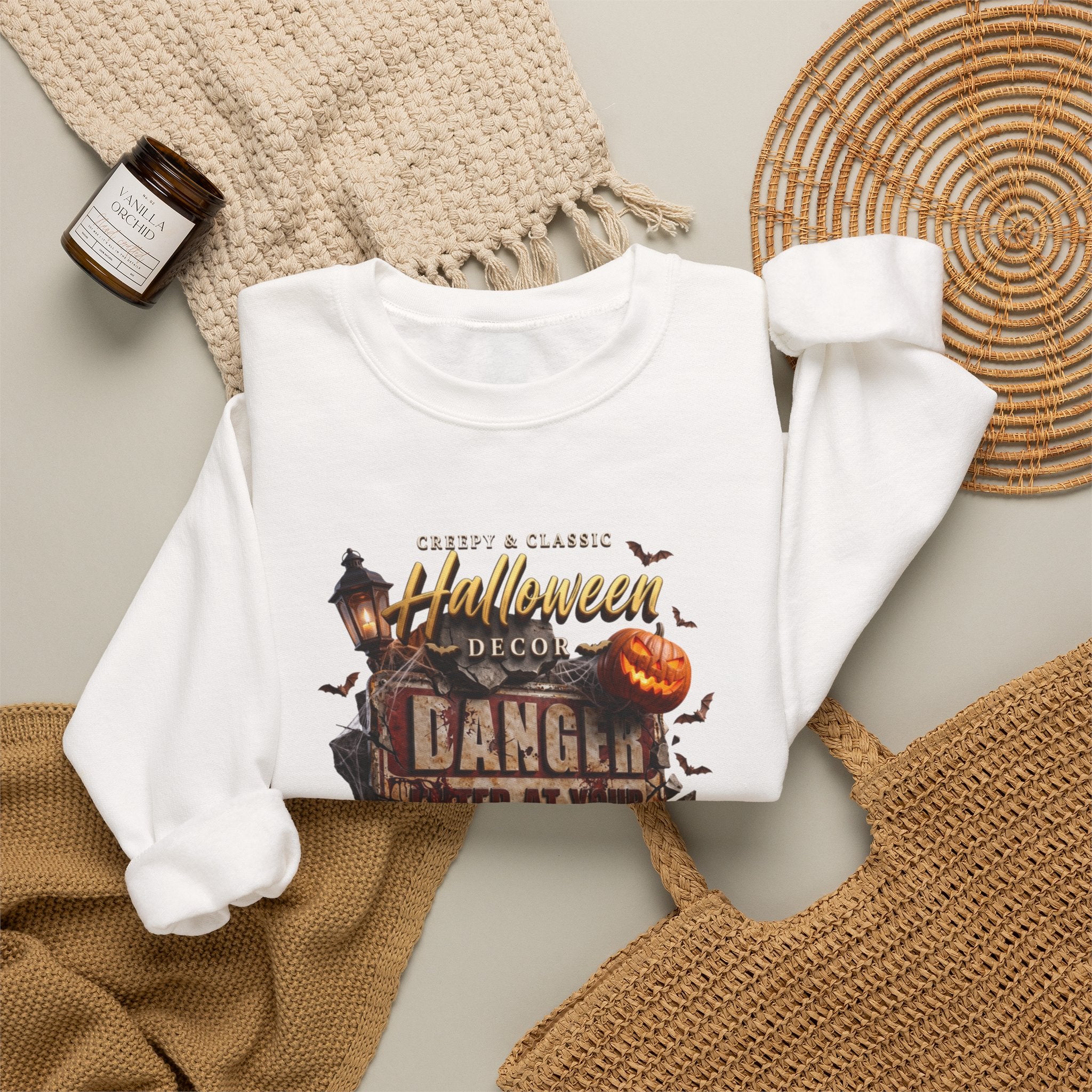White crewneck sweatshirt styled flat with a candle — aged Danger sign over glowing pumpkins