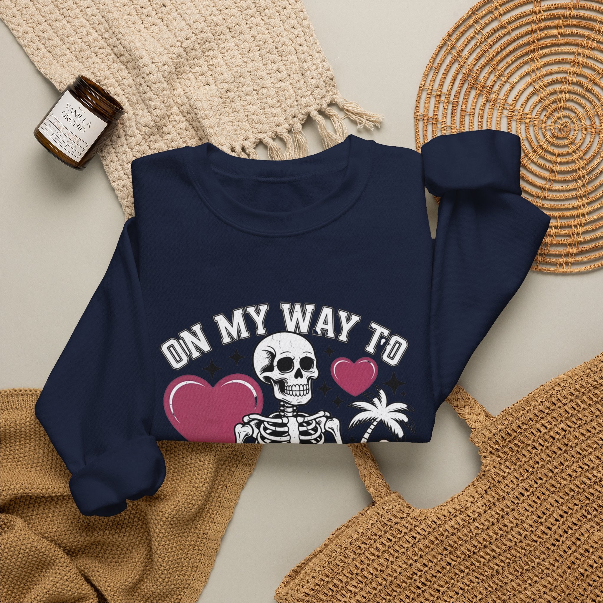 Navy crewneck sweatshirt styled flat with a candle — line-drawn skeletons under pink hearts
