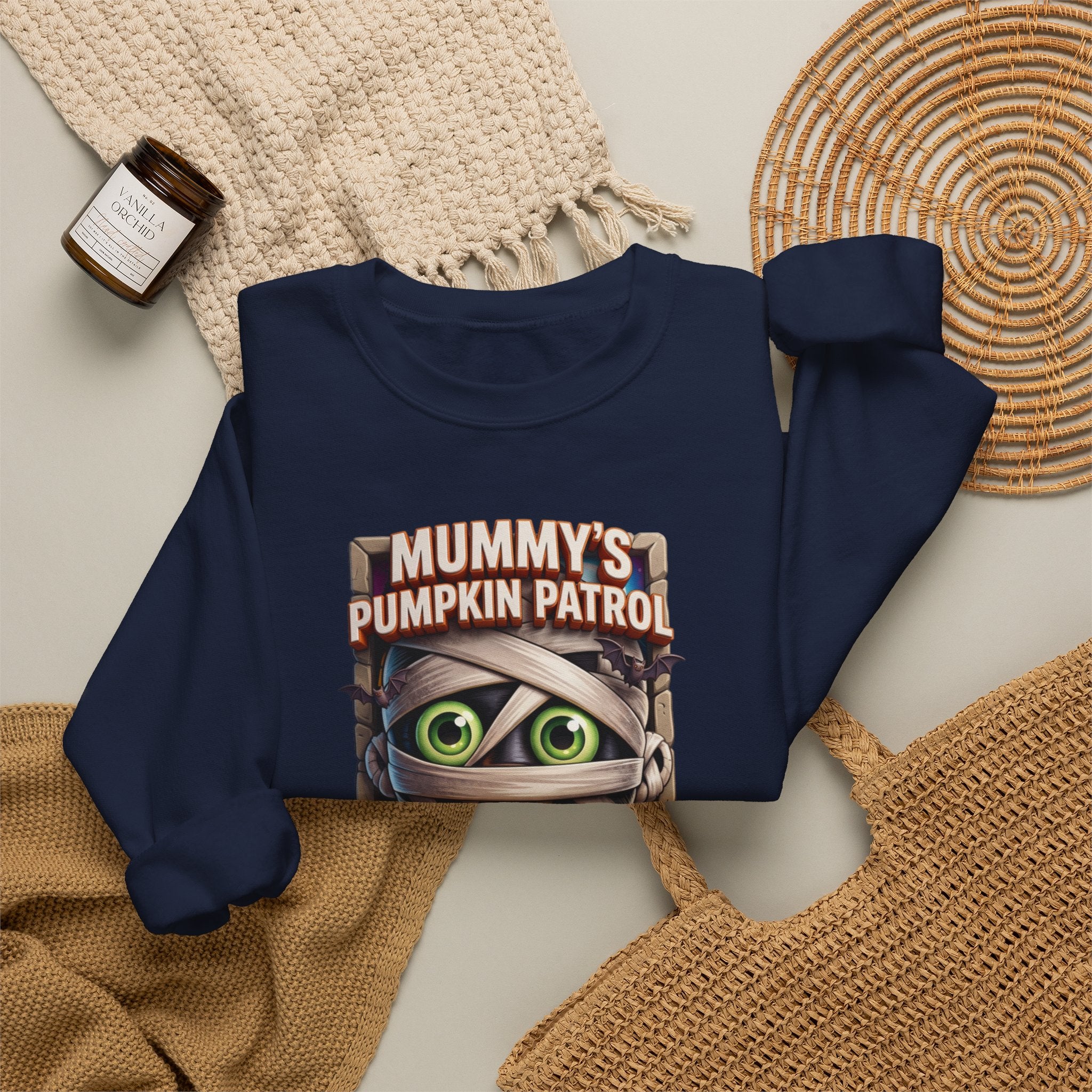 Navy crewneck sweatshirt styled flat with a candle — cartoon mummy hugging a carved pumpkin