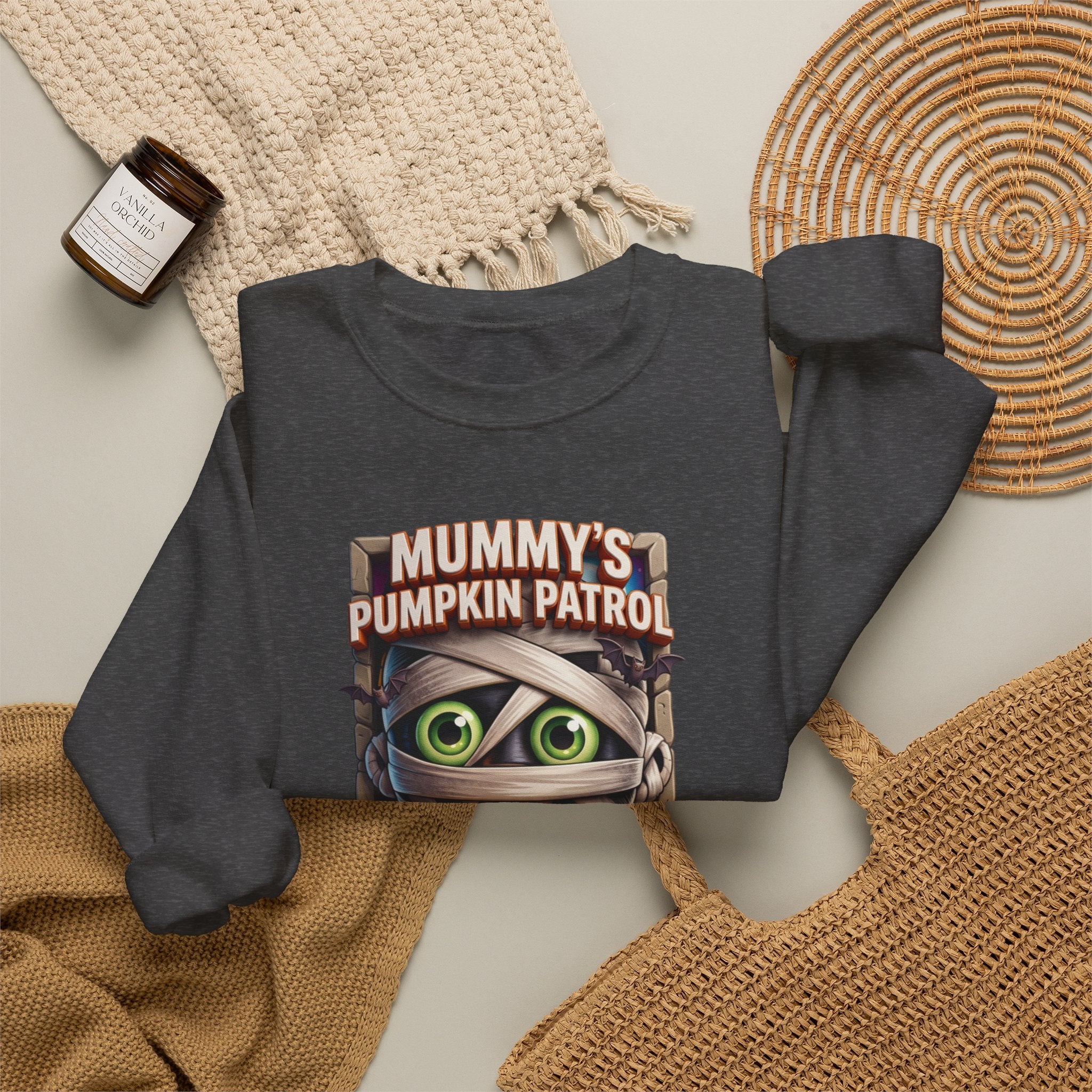 Dark Heather crewneck sweatshirt styled flat with a candle — cartoon mummy hugging a carved pumpkin