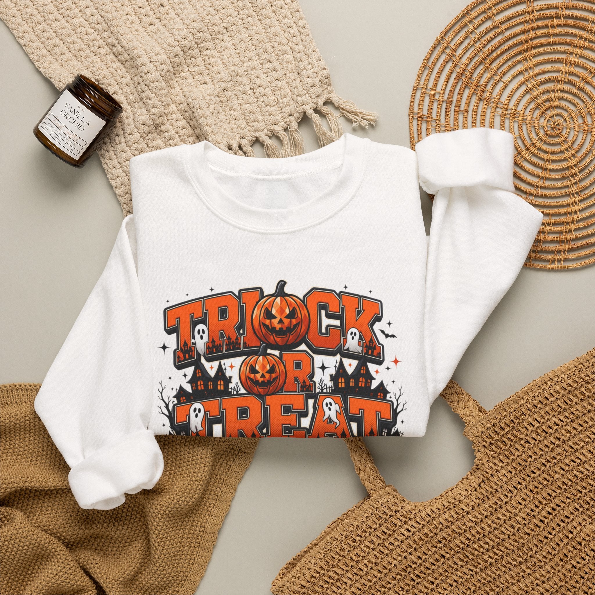 White crewneck sweatshirt styled flat with a candle — stacked orange and black lettering
