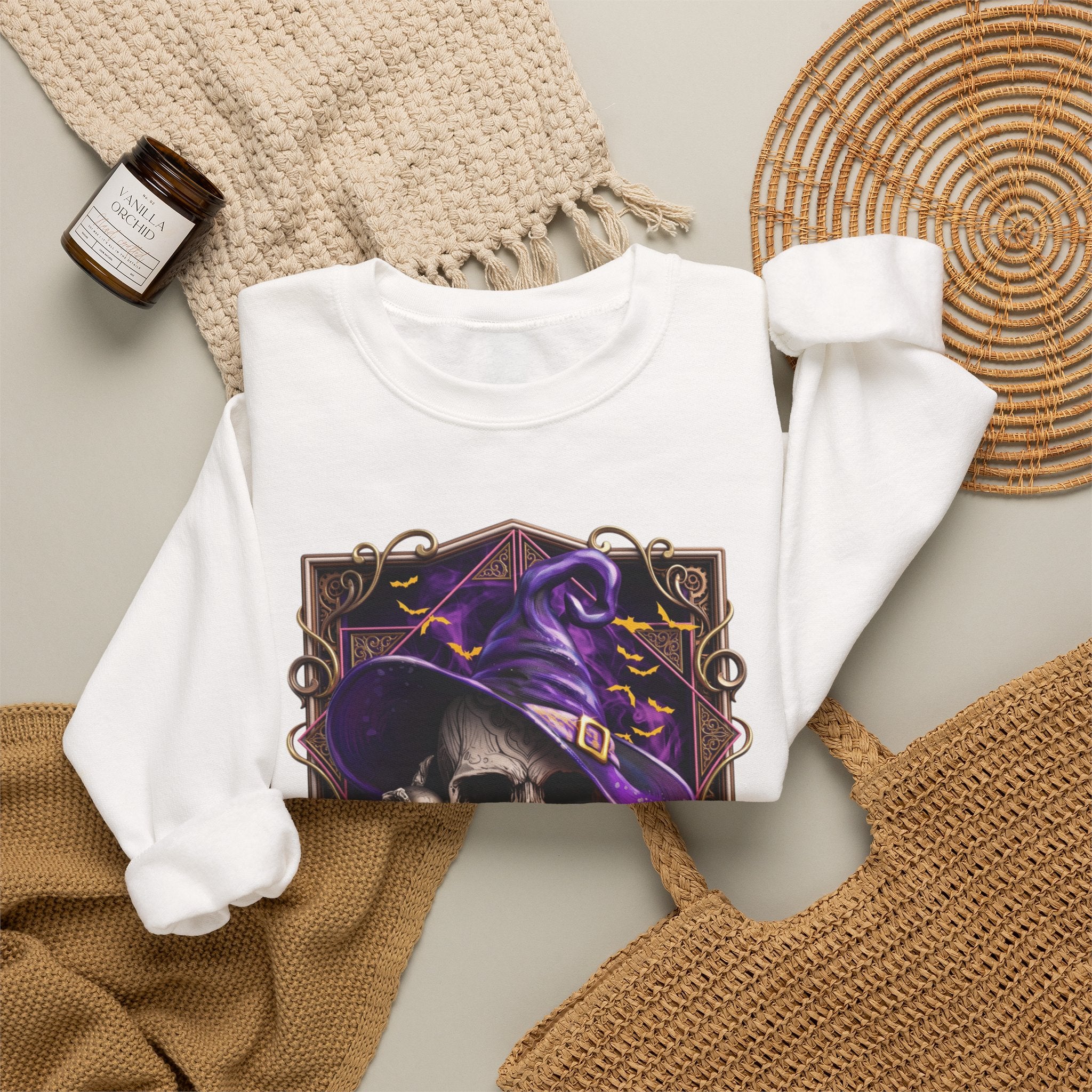 White crewneck sweatshirt styled flat with a candle — skull in a purple witch hat