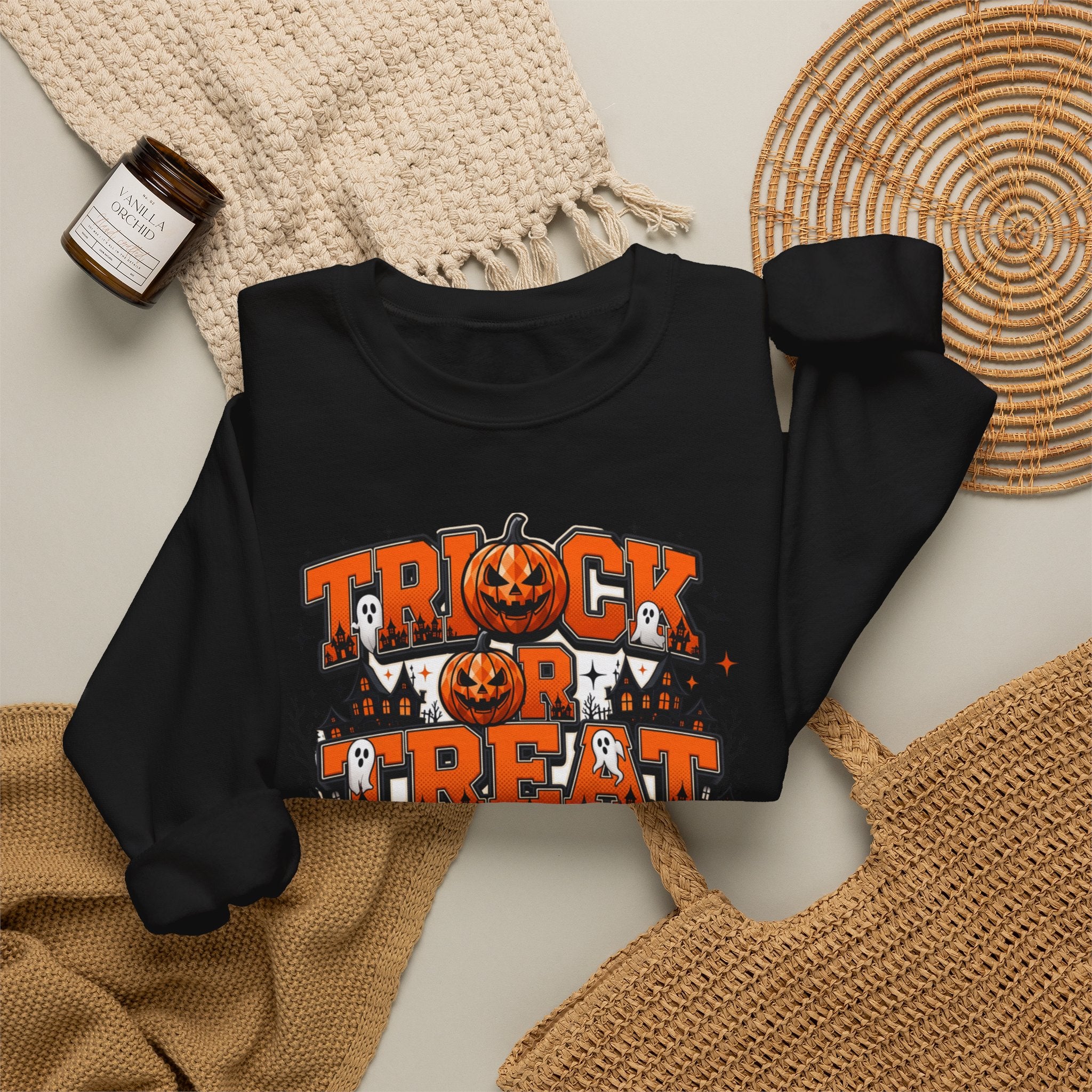 Black crewneck sweatshirt styled flat with a candle — stacked orange and black lettering