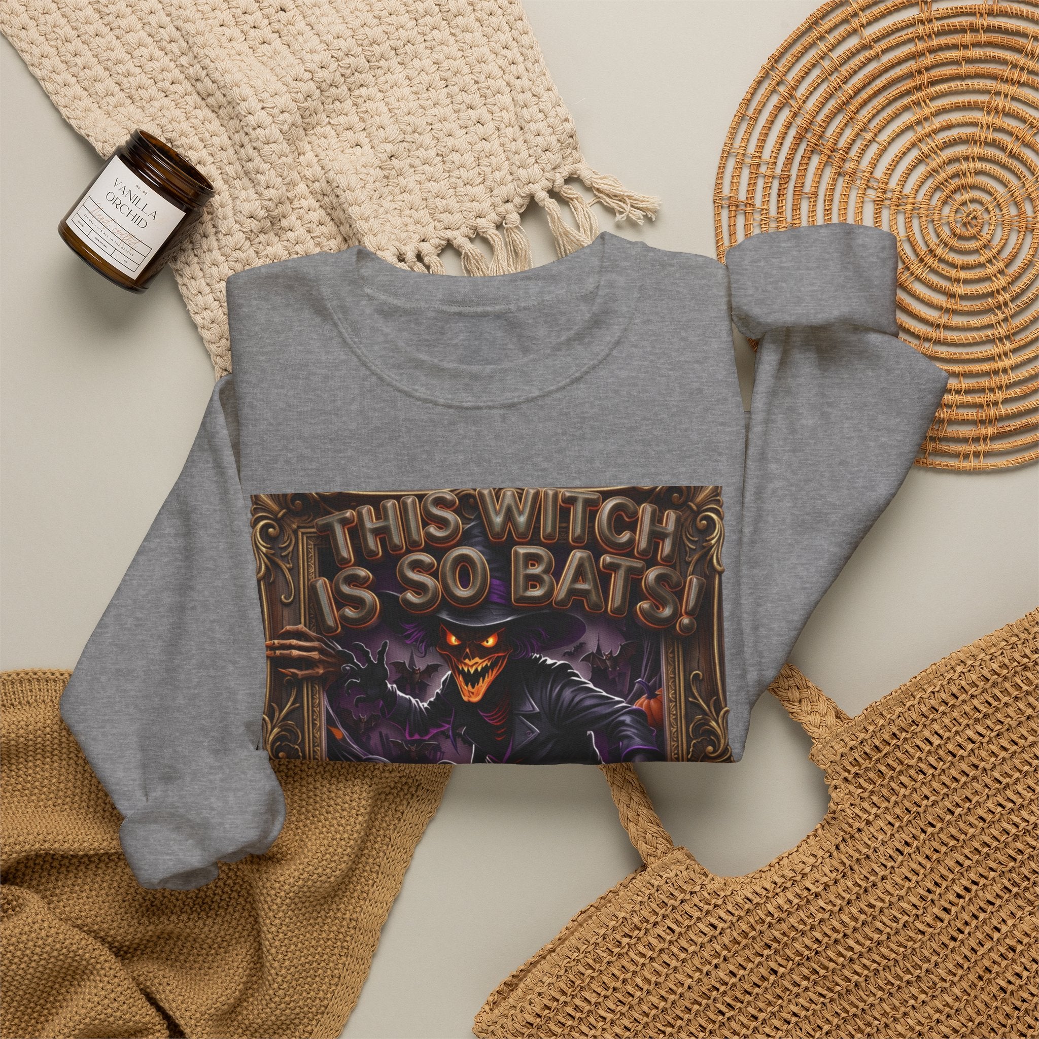 Graphite Heather crewneck sweatshirt styled flat with a candle — grinning witch in a pointed hat
