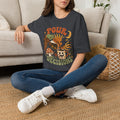 Dark Heather Grey t-shirt laid flat, printed with a green witch hand tipping a flower-patterned coffee pot into