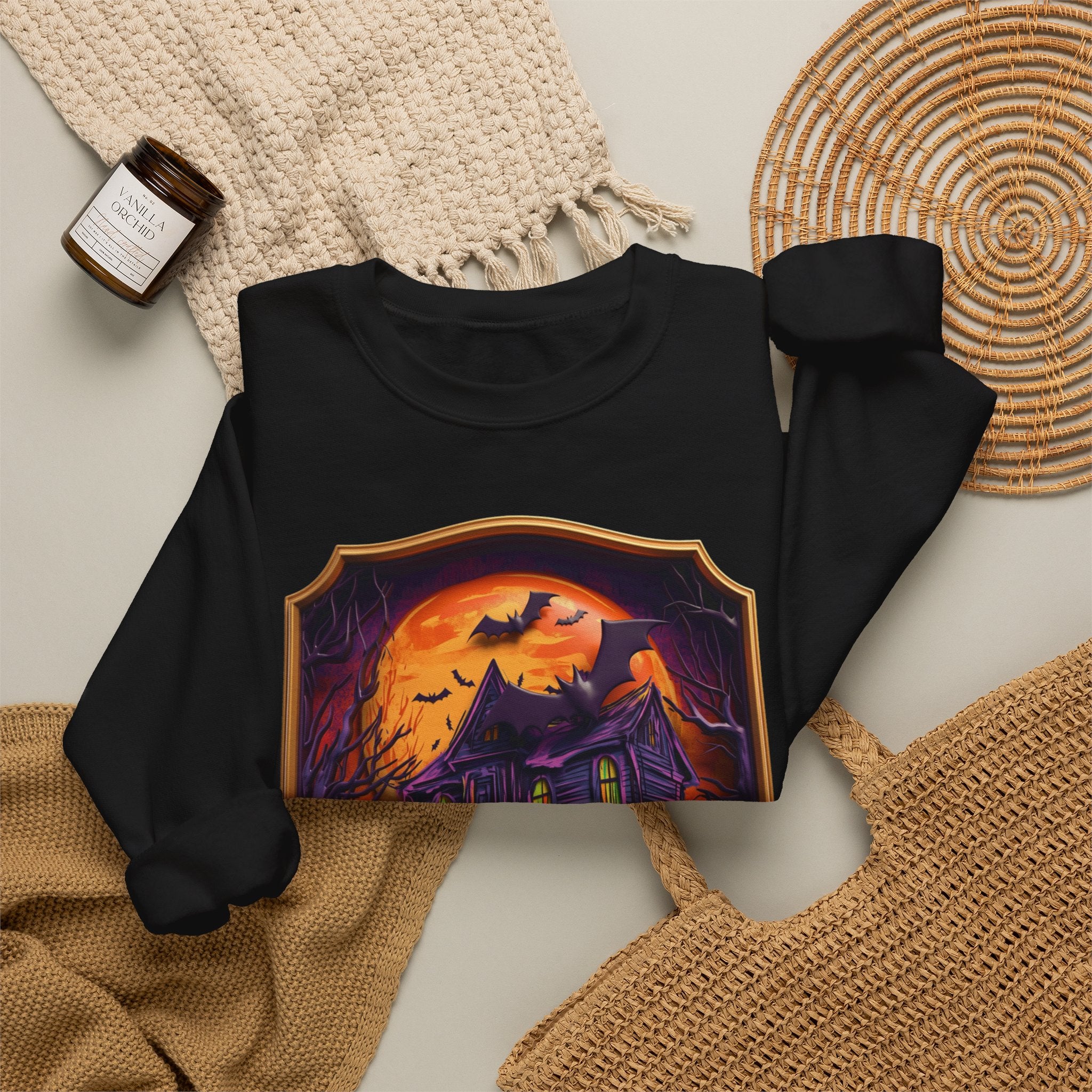 Black crewneck sweatshirt styled flat with a candle — haunted mansion under an orange moon