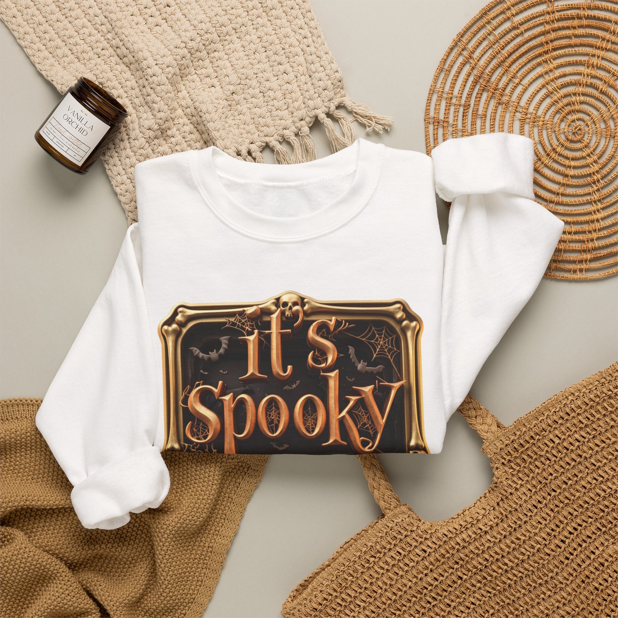 White crewneck sweatshirt styled flat with a candle — copper It's Spooky Season lettering