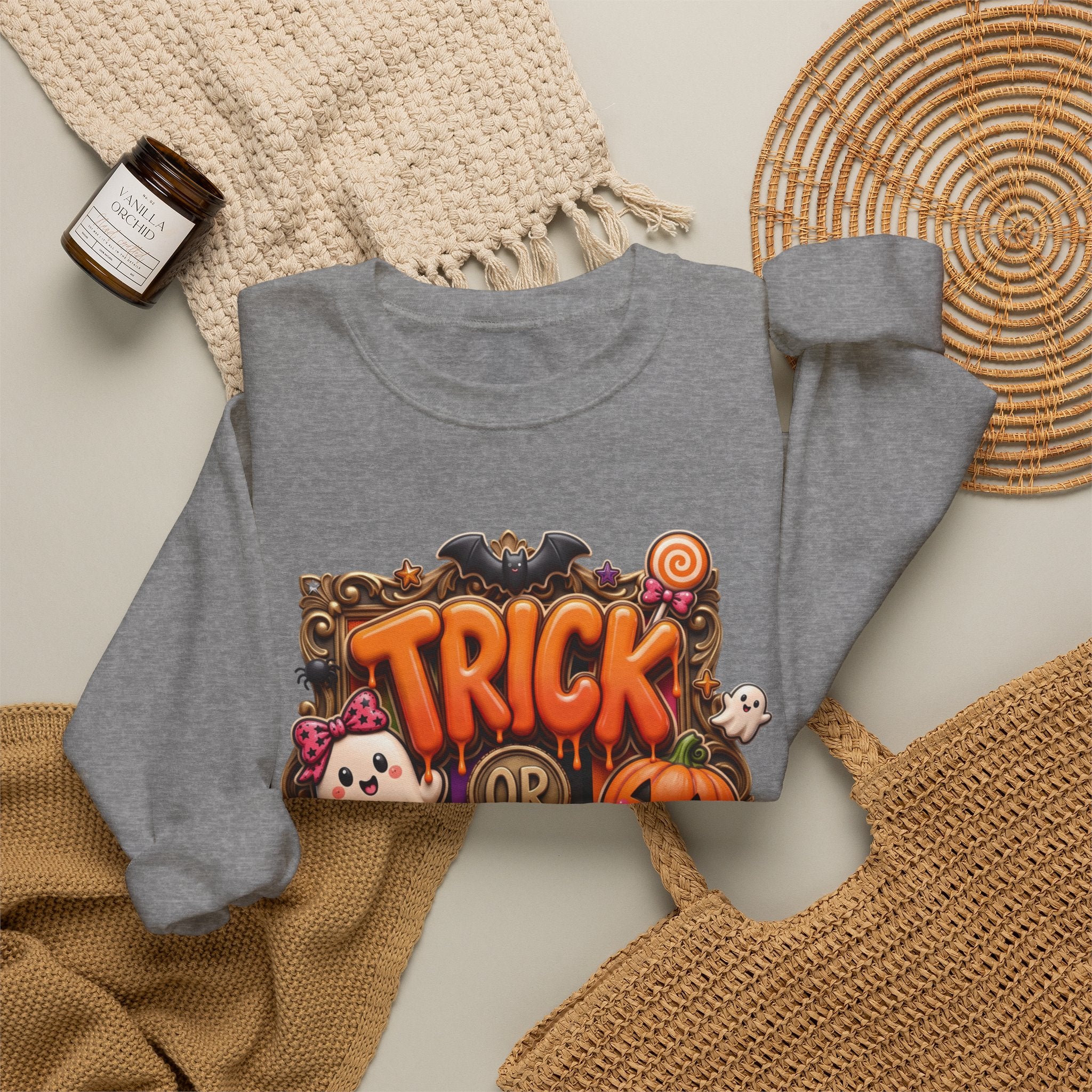 Graphite Heather crewneck sweatshirt styled flat with a candle — puffy orange trick or treat lettering