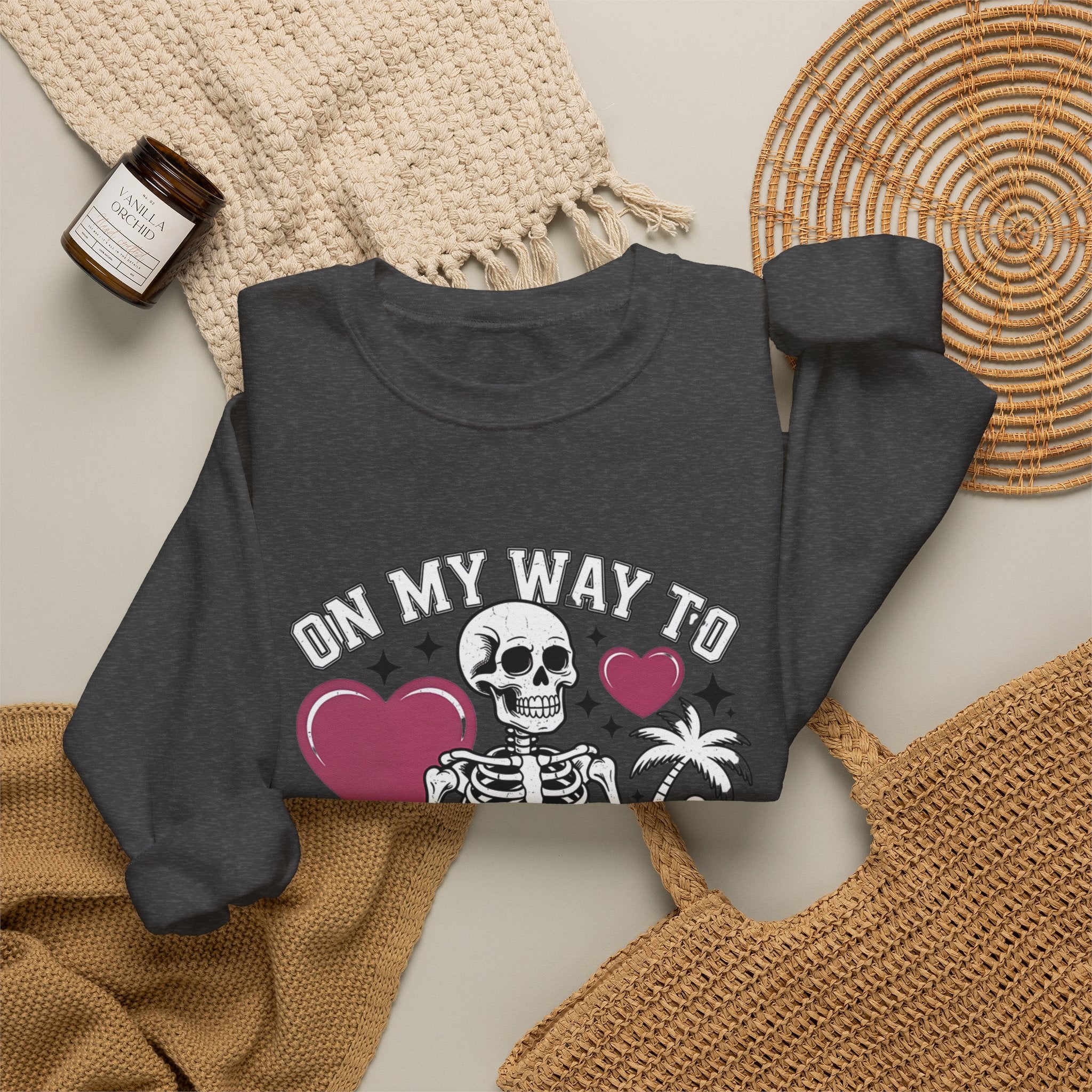 Dark Heather crewneck sweatshirt styled flat with a candle — line-drawn skeletons under pink hearts