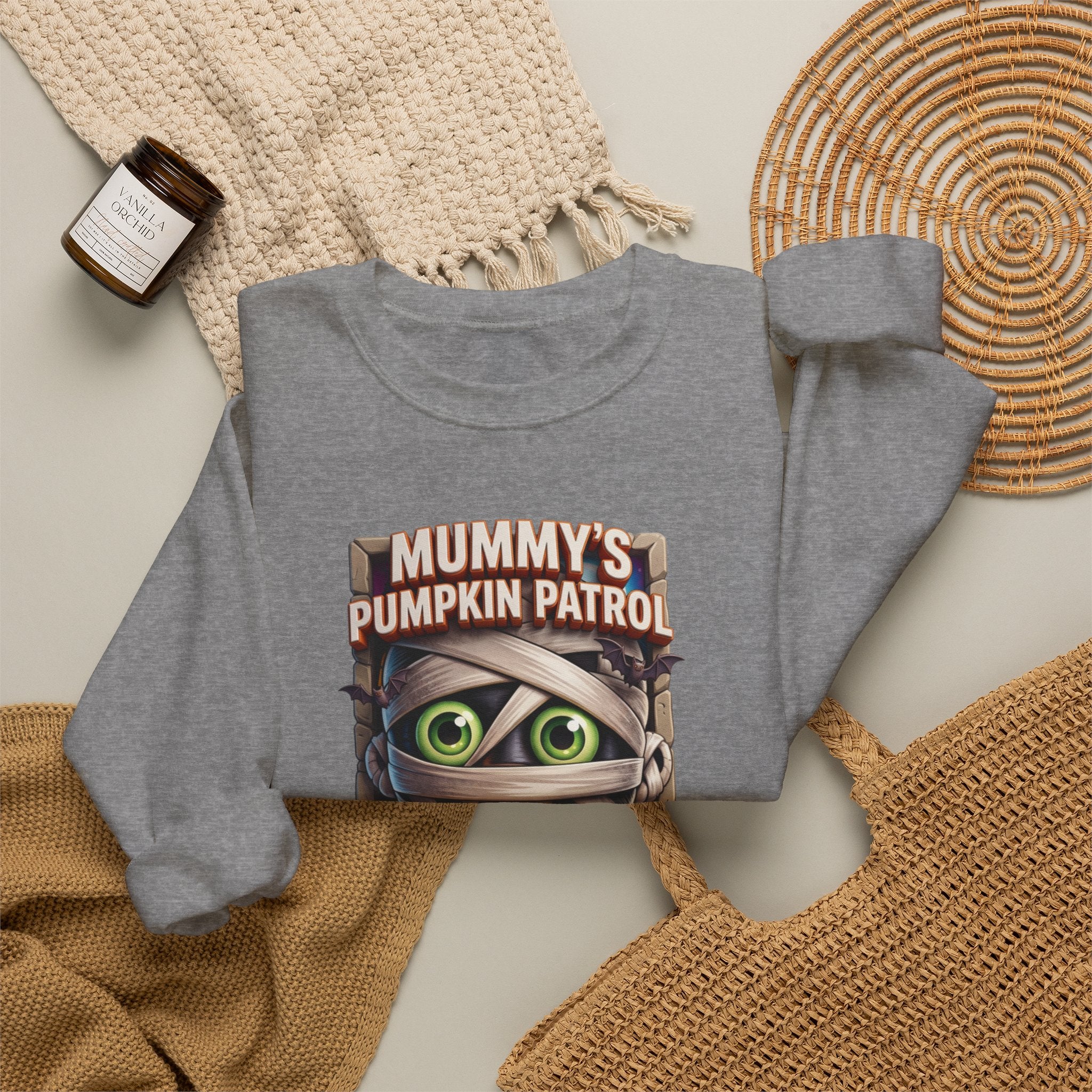 Graphite Heather crewneck sweatshirt styled flat with a candle — cartoon mummy hugging a carved pumpkin