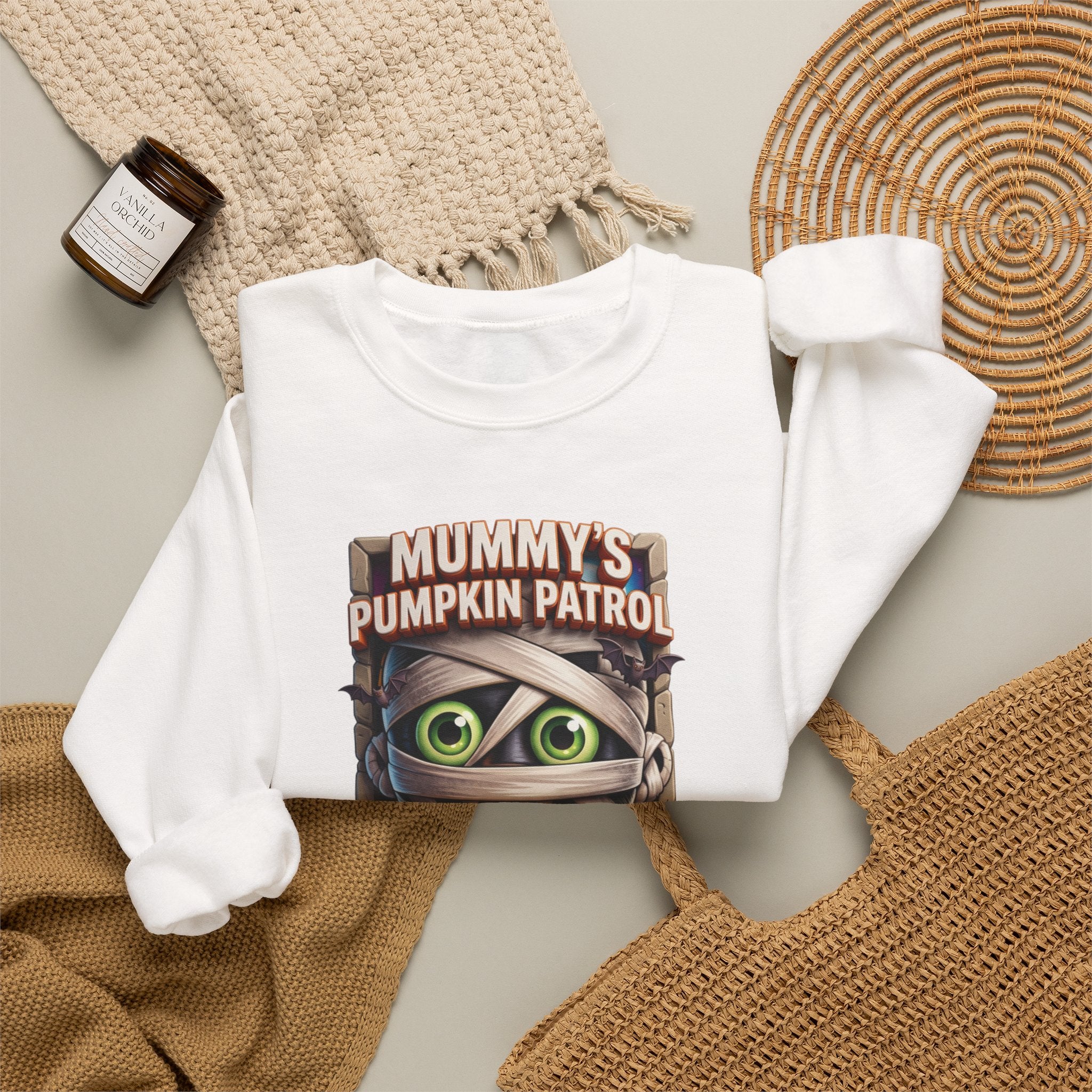 White crewneck sweatshirt styled flat with a candle — cartoon mummy hugging a carved pumpkin